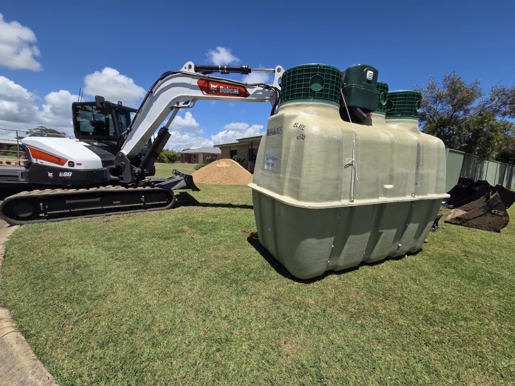 An excavator beside a wastewater treatment tank on a mown lawn