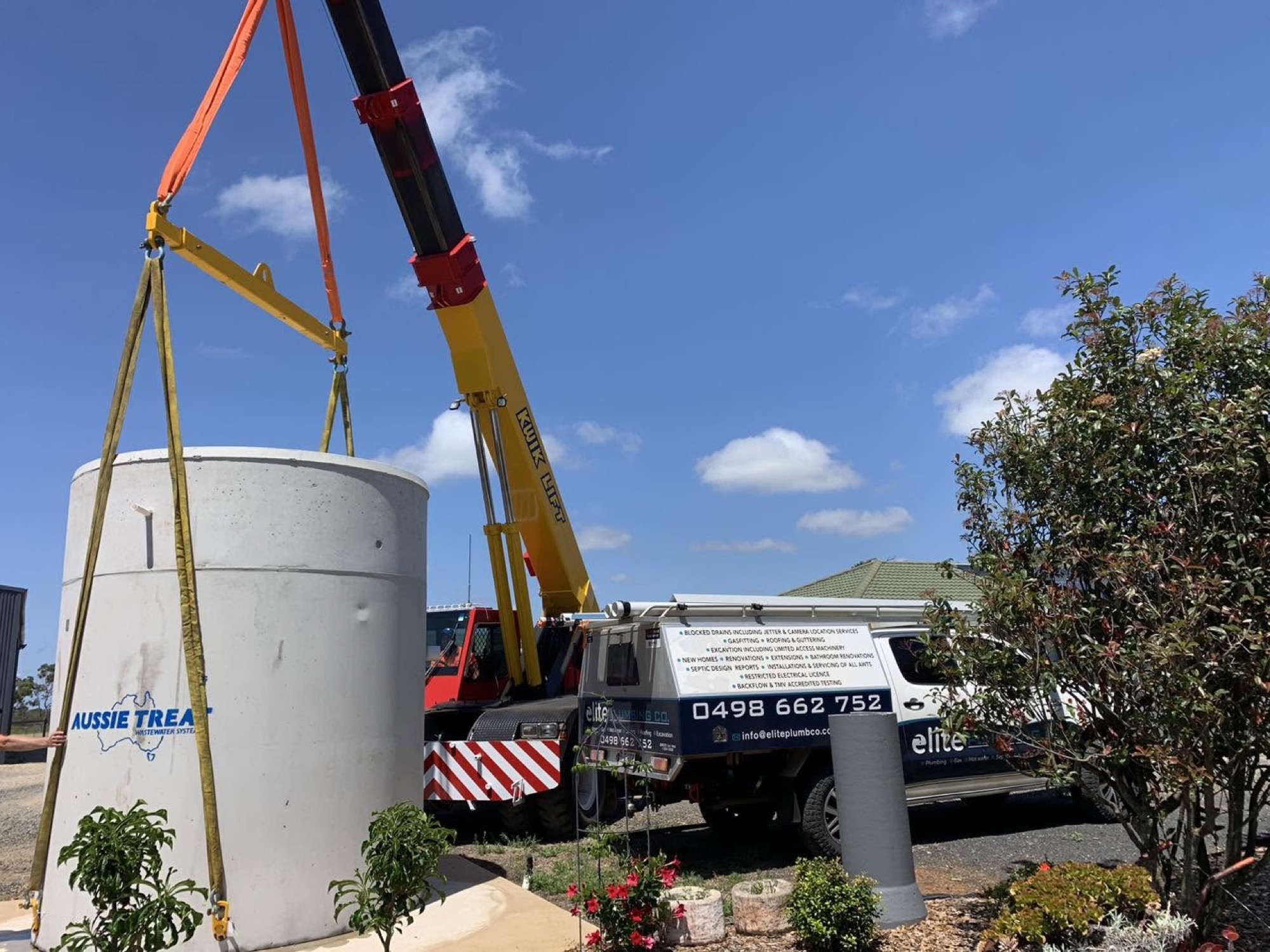 A crane lifting a round concrete tank beside a branded truck