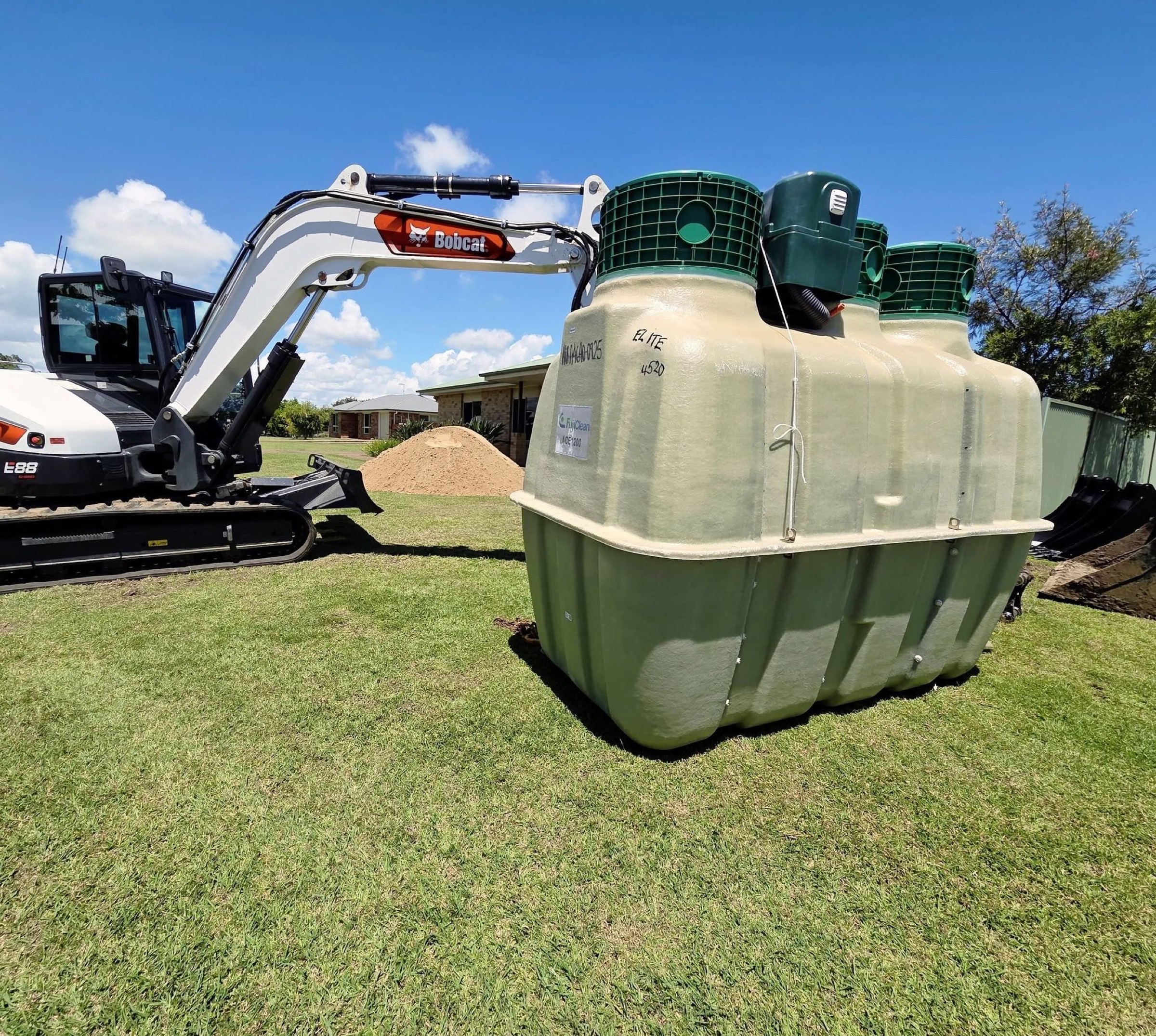 An excavator beside a large wastewater treatment tank on a grassed block