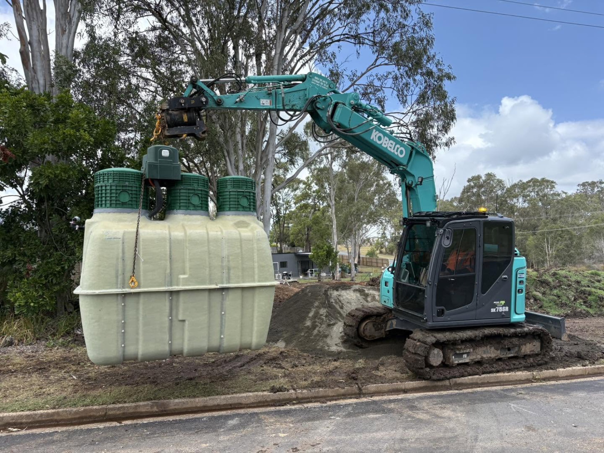 An excavator and treatment tanks on a roadside verge