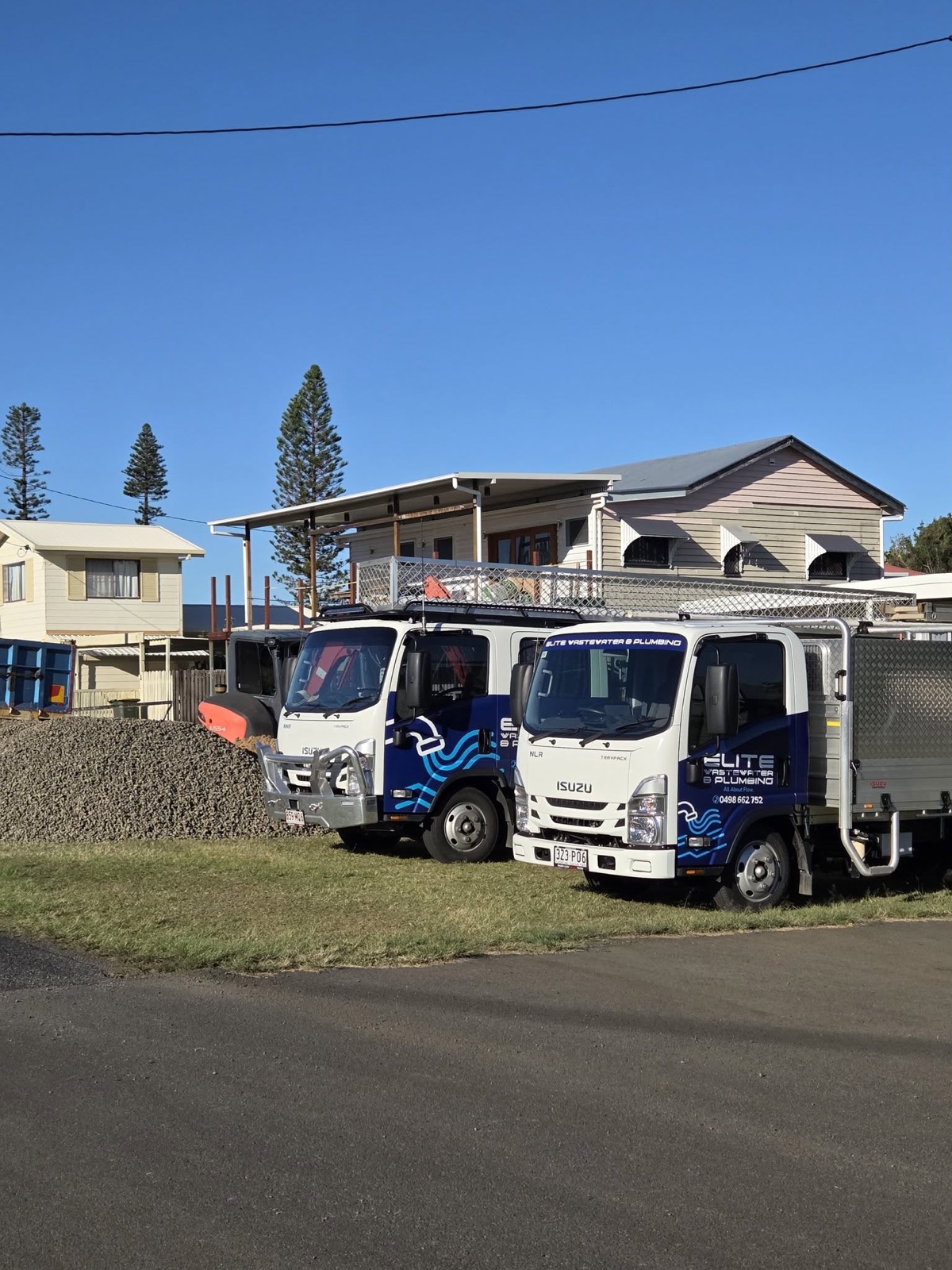 Two branded Elite Wastewater and Plumbing trucks parked on a grass verge