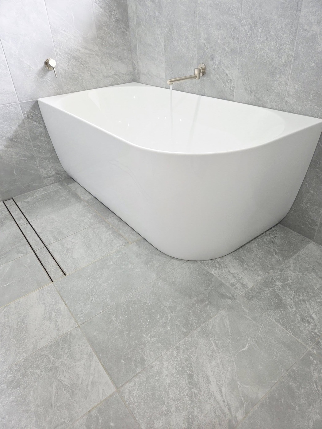 A freestanding bath on large-format floor tiles in a finished bathroom