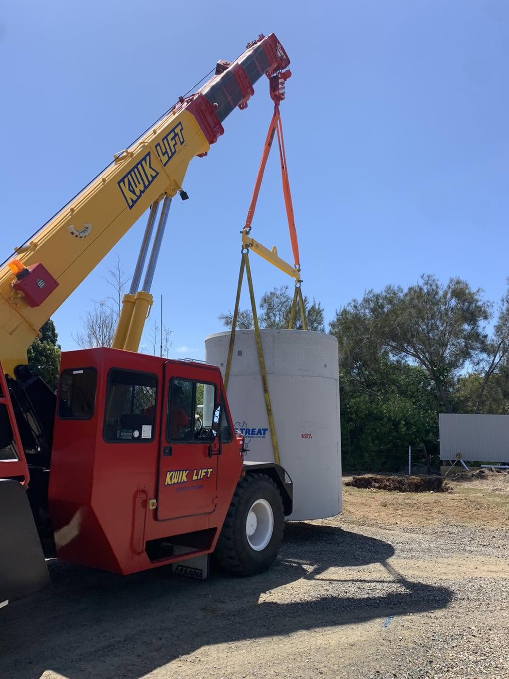A crane truck lifting a tall concrete tank into place on a work site