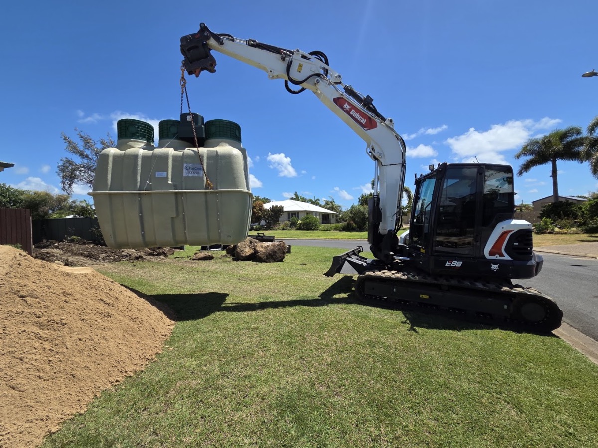 An excavator beside three wastewater treatment tanks on a lawn