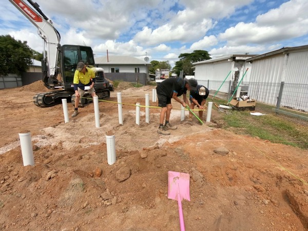 Two workers on a residential site with pipe stubs set into the ground