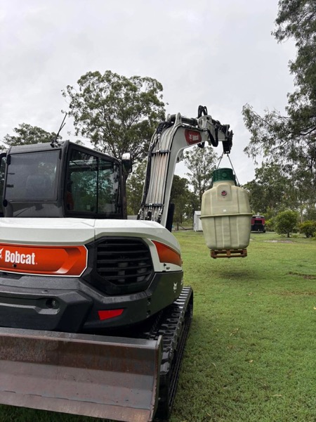 A compact excavator on a grassed block with a tank behind it