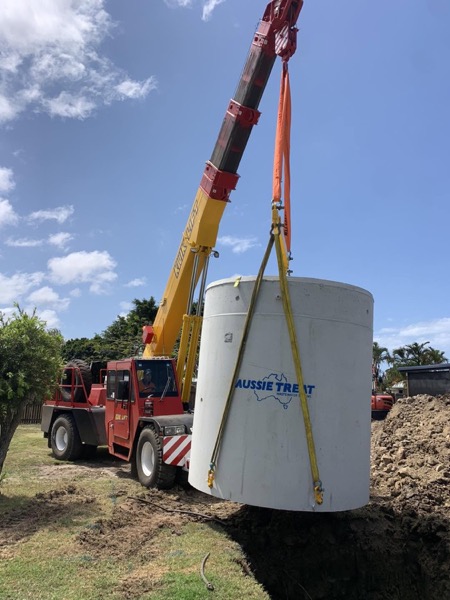 A crane lifting a tall concrete tank at a work site