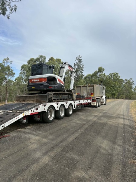 A truck and trailer carrying an excavator on a country road