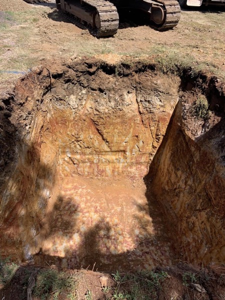 A deep excavation pit cut through red soil