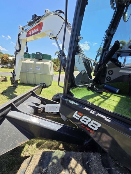 A tracked excavator on a lawn with treatment tanks behind it
