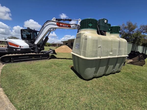 An excavator beside a treatment tank on a mown lawn