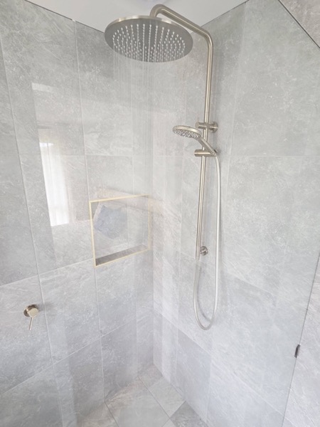 A tiled shower with a rail shower and a recessed niche