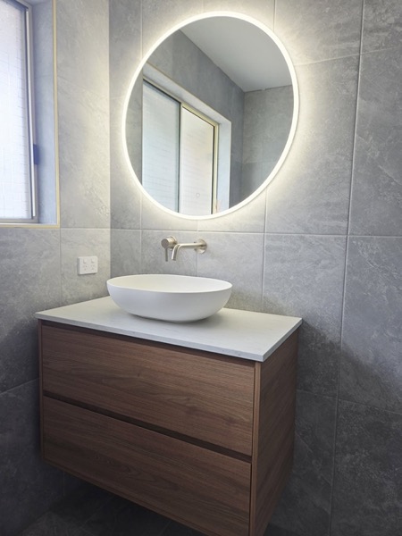 A finished bathroom vanity with a basin and round mirror