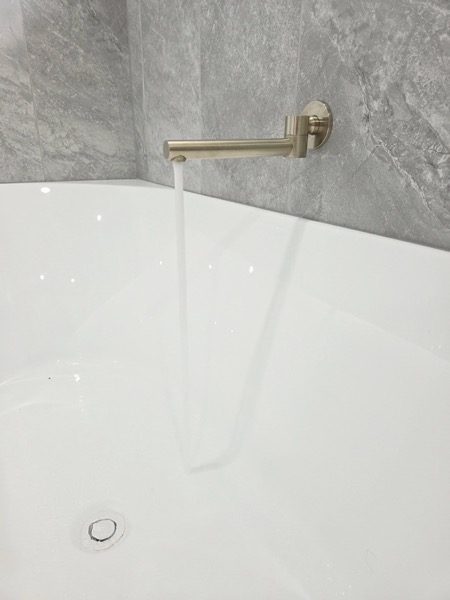A wall-mounted bath spout above a white bath